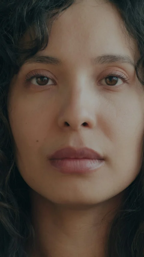 A close-up portrait of a woman with curly dark hair and brown eyes