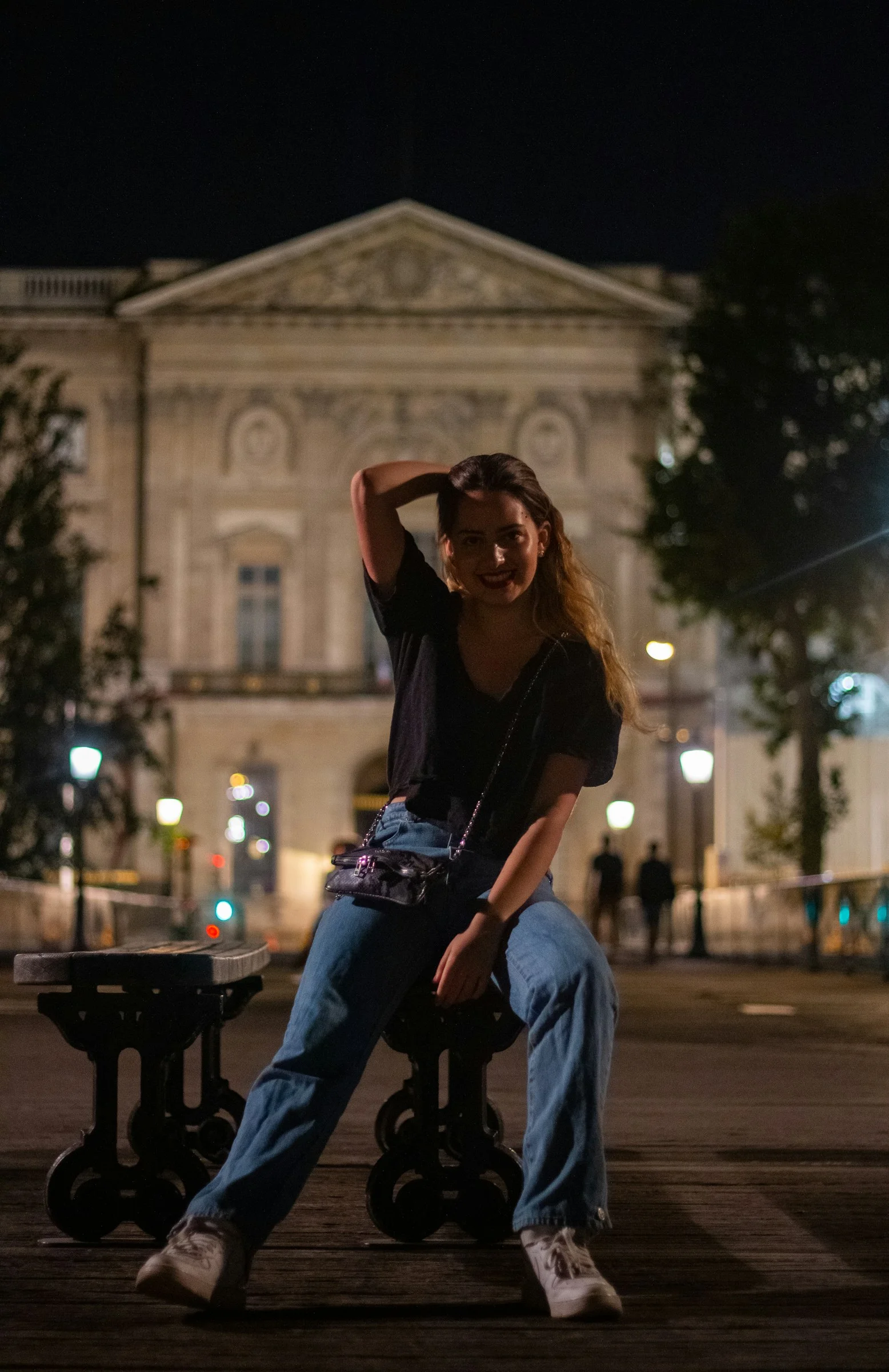 woman in black shirt and blue denim jeans sitting on brown wooden bench during night time