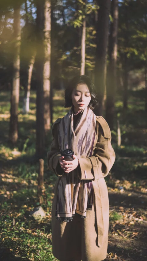 A woman standing in the woods wearing a long coat