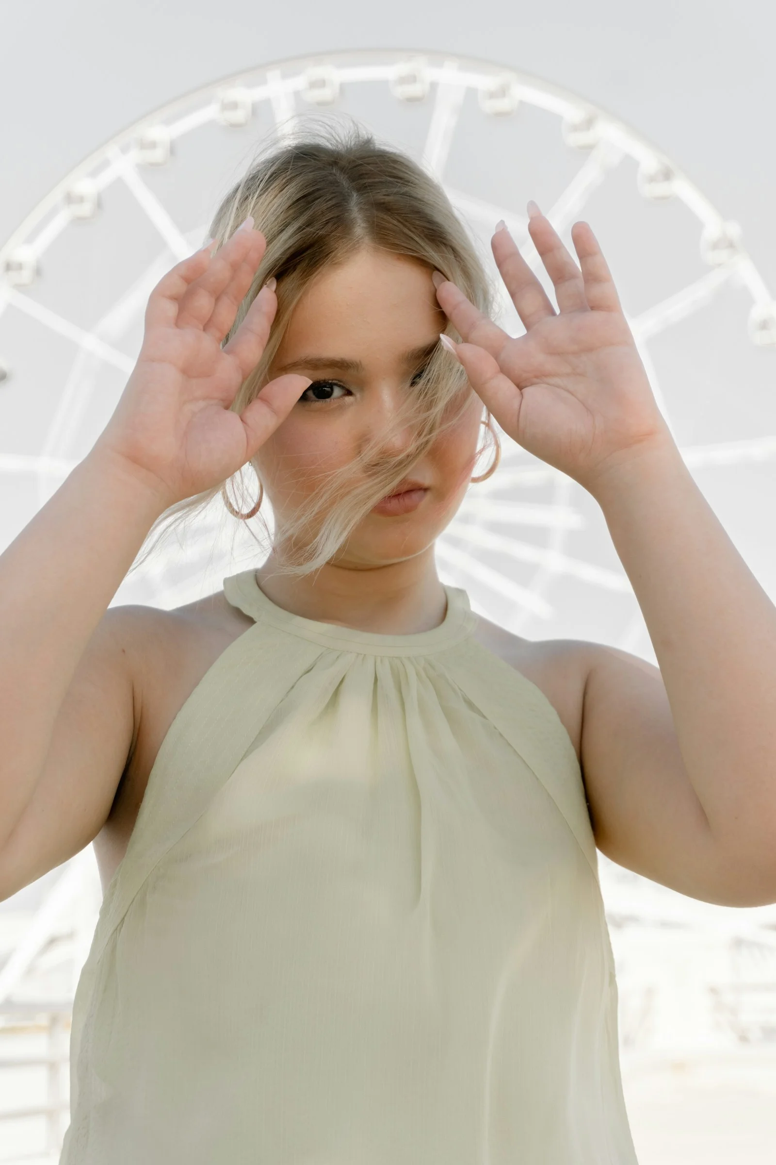 A young woman with blonde hair holding her hands up before a ferris wheel