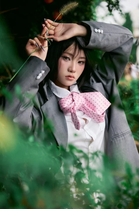 Young woman in blazer and pink tie among green foliage