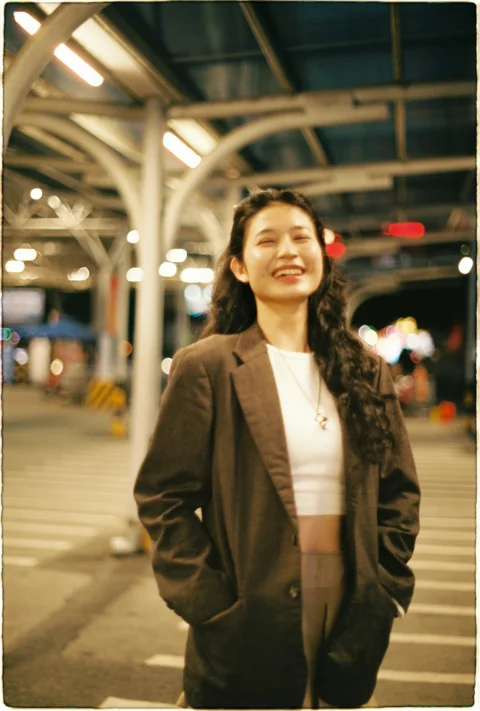 Young woman in a brown blazer smiling at night