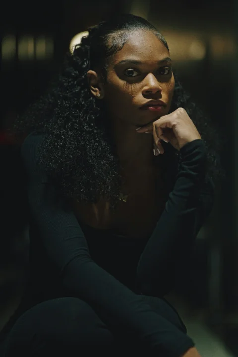 A young woman with curly hair poses thoughtfully