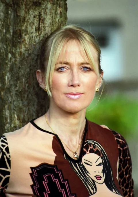 Blonde woman with blue eyes leaning against tree