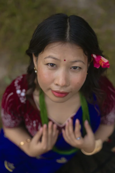 A woman in a dark red and blue dress with a pink flower in her hair