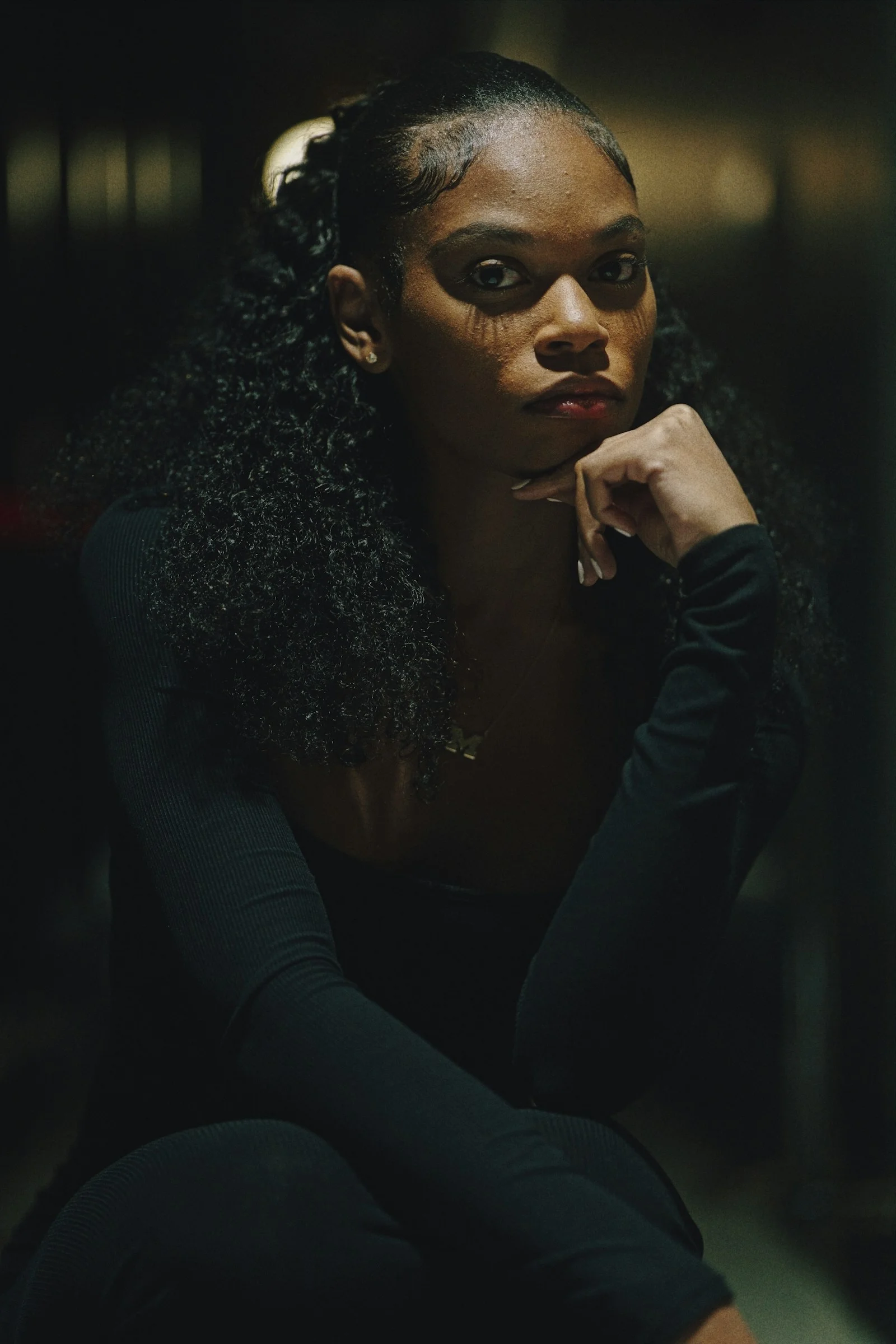 A young woman with curly hair poses thoughtfully