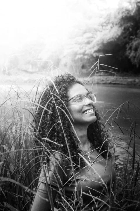 Smiling woman with curly hair and glasses among tall grass