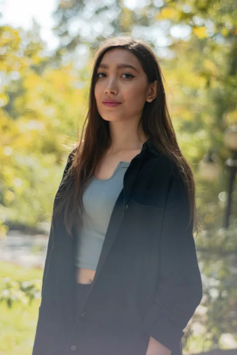 Young woman standing outdoors with blurred trees behind her