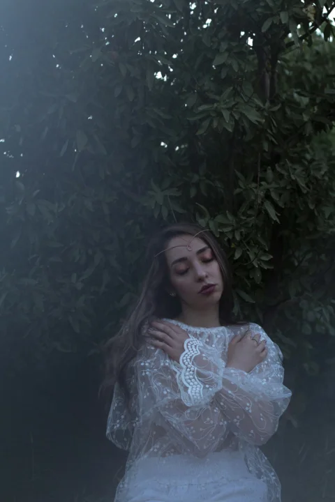 a woman in a white dress standing in front of a tree