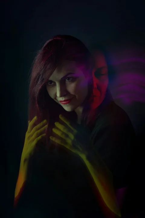 A woman standing in the dark with her hands on her chest