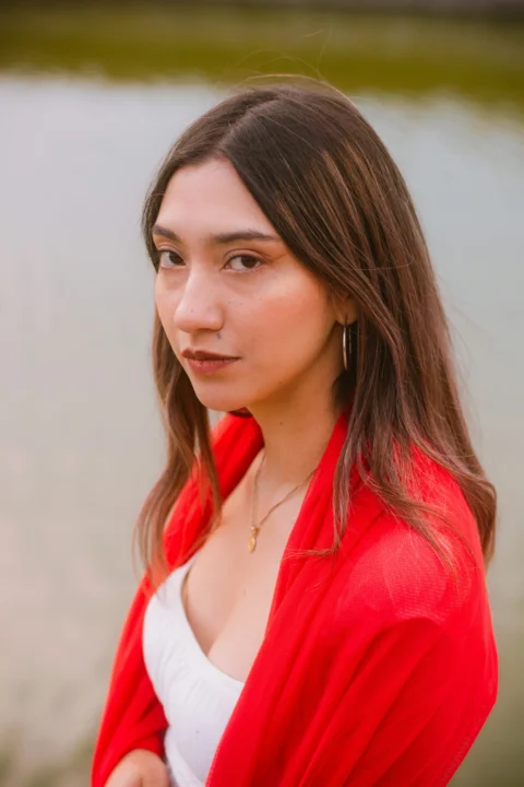 Young woman in red jacket looking at camera by water