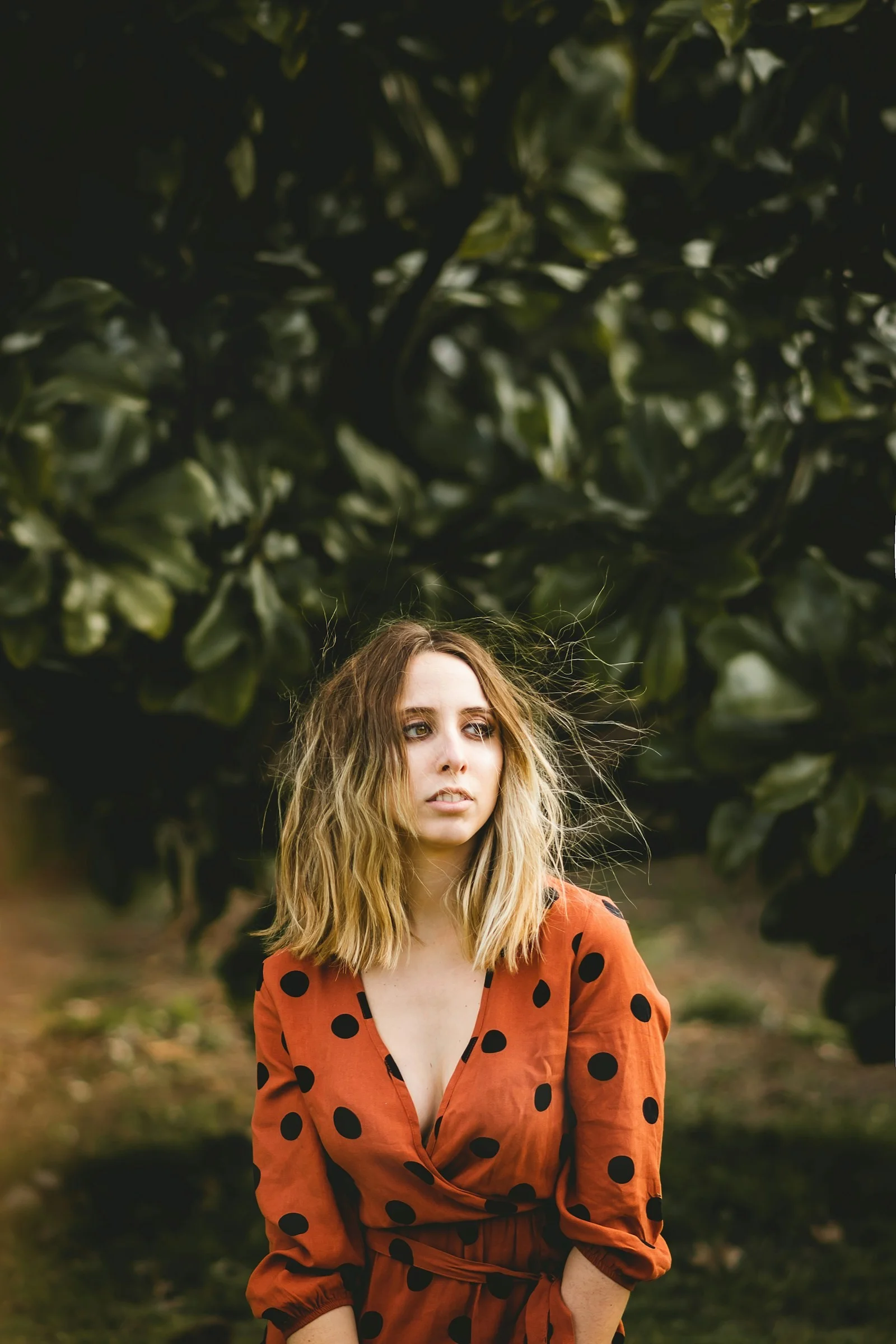 woman in orange coat standing near green tree during daytime