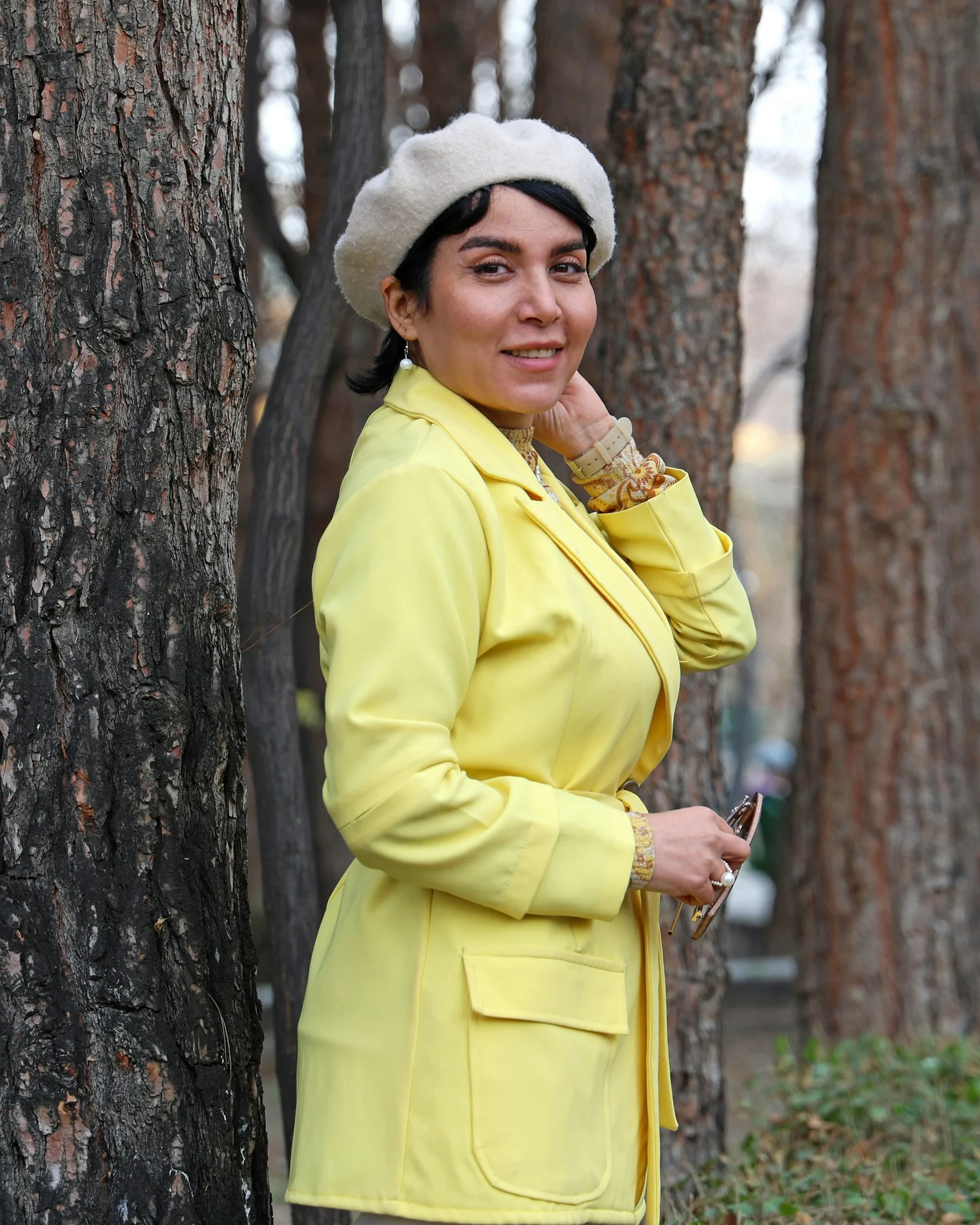 Woman in yellow jacket and beret poses outdoors