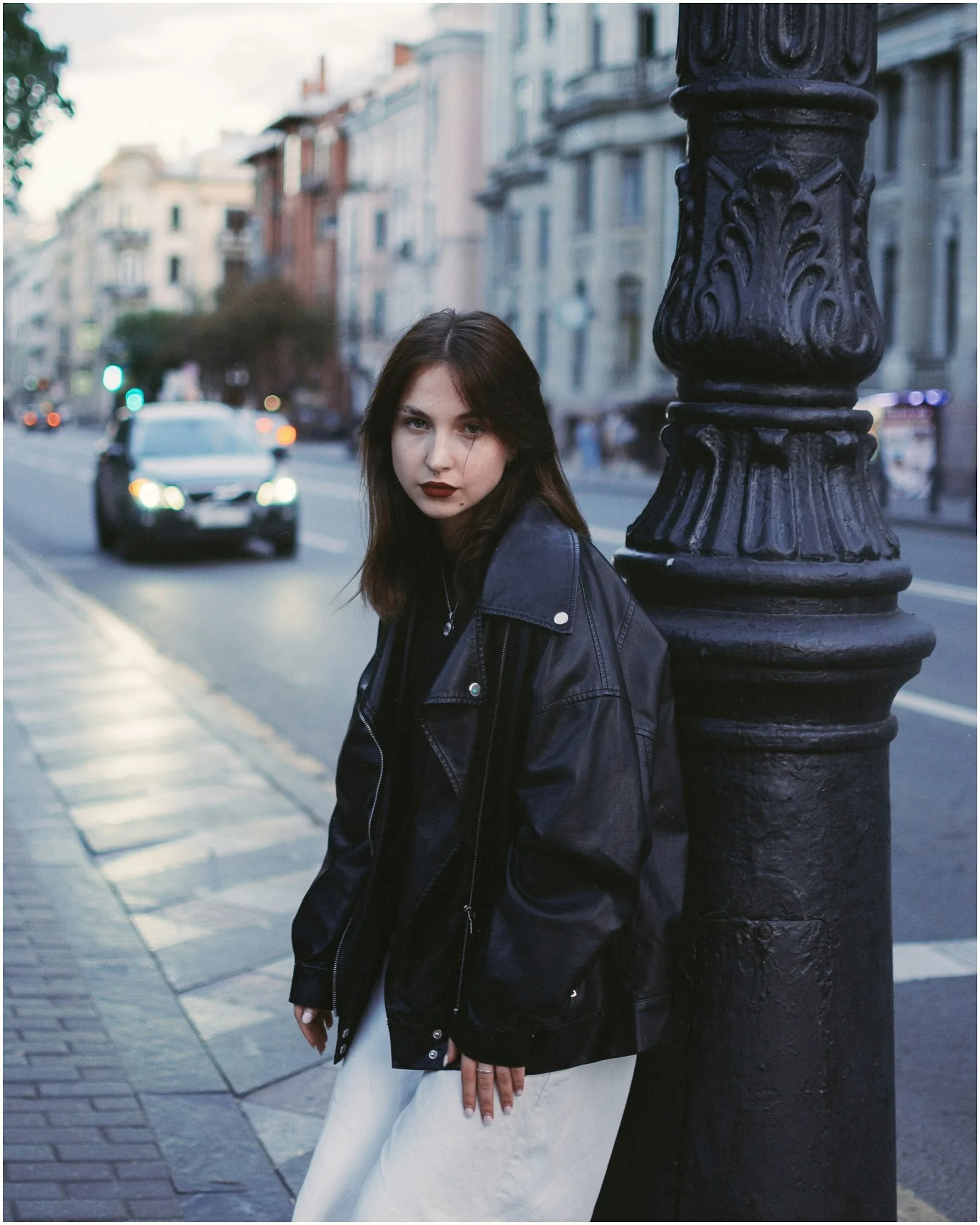 a woman leaning against a pole on a city street