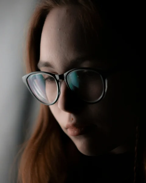 A woman wearing glasses looking down at her cell phone