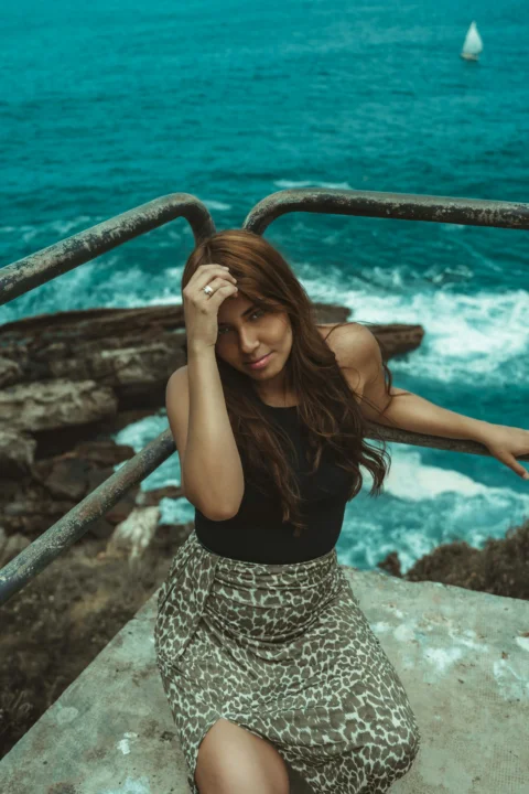 a beautiful woman sitting on top of a metal rail next to the ocean