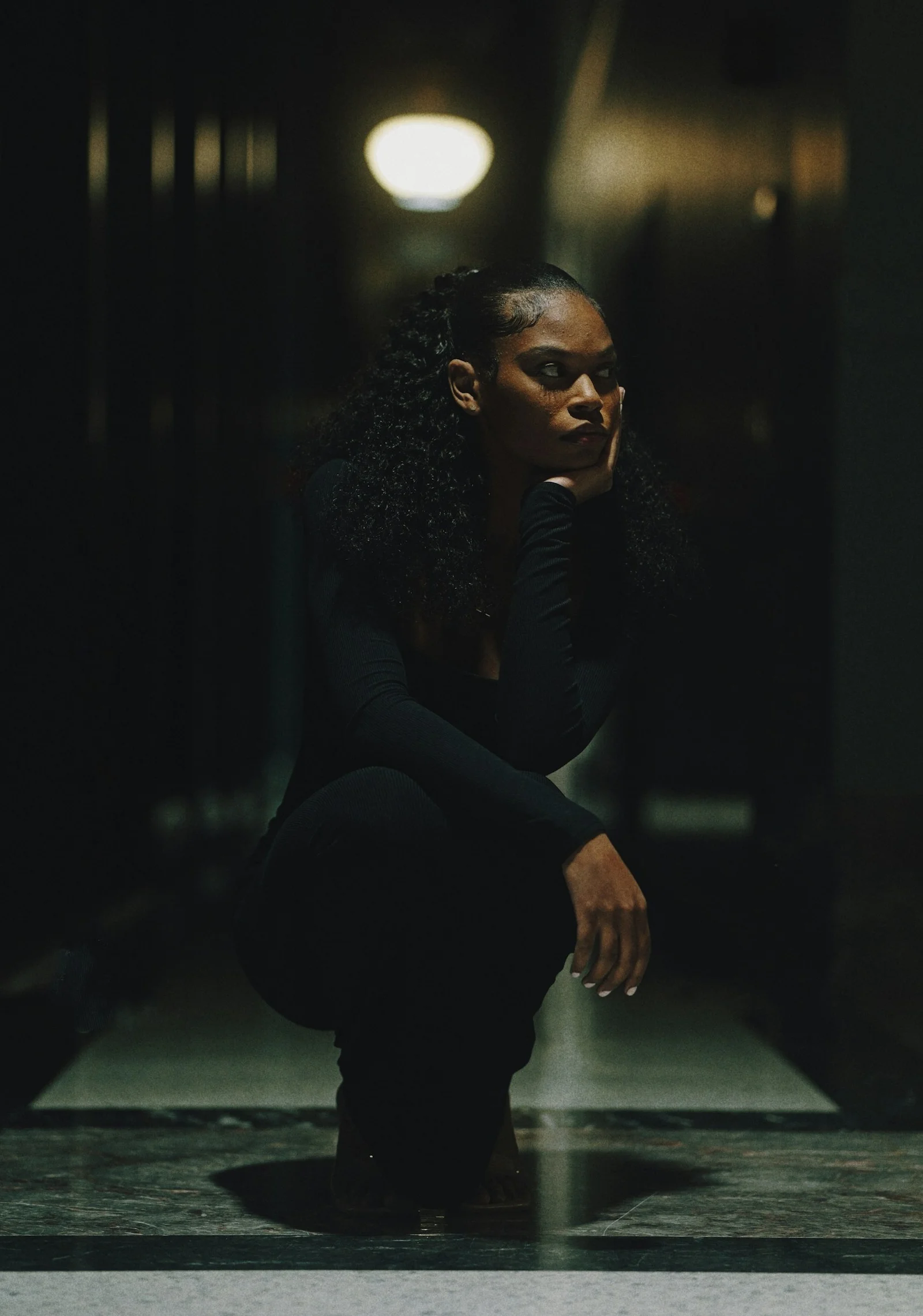 A woman in black clothing crouching in a dark hallway