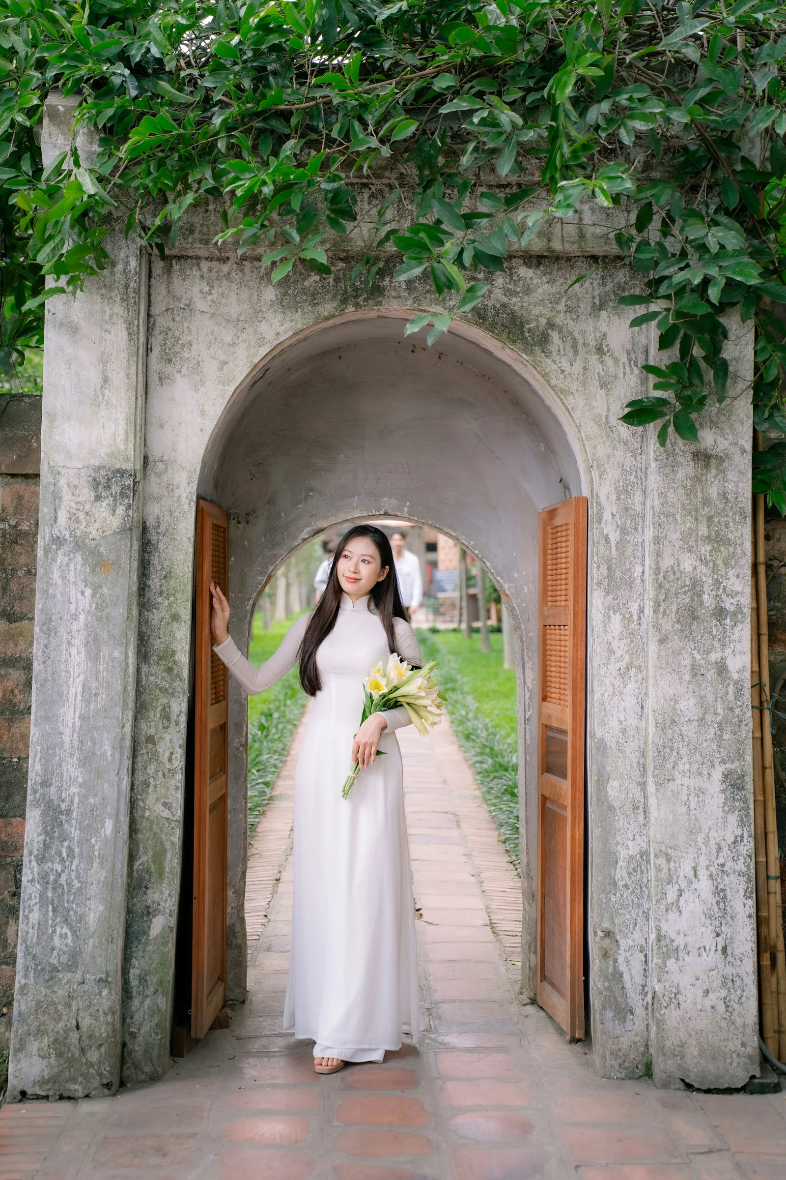 A woman in white stands at a stone archway