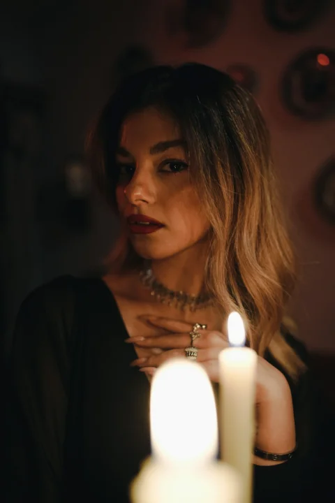 A woman in a black dress with jewelry lit by a candle flame