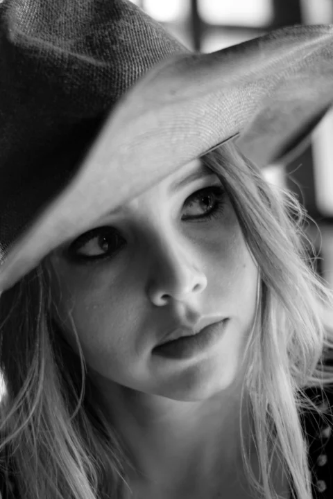 A woman gazes thoughtfully, wearing a hat