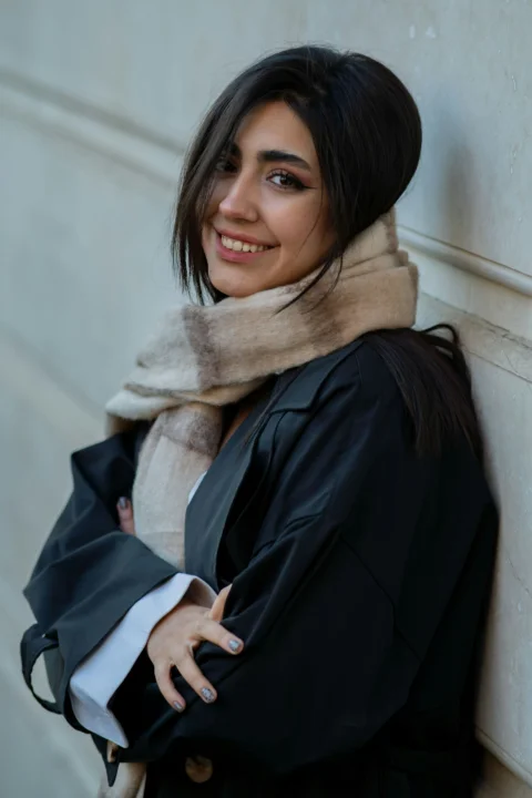 A smiling woman in a scarf leans against a wall