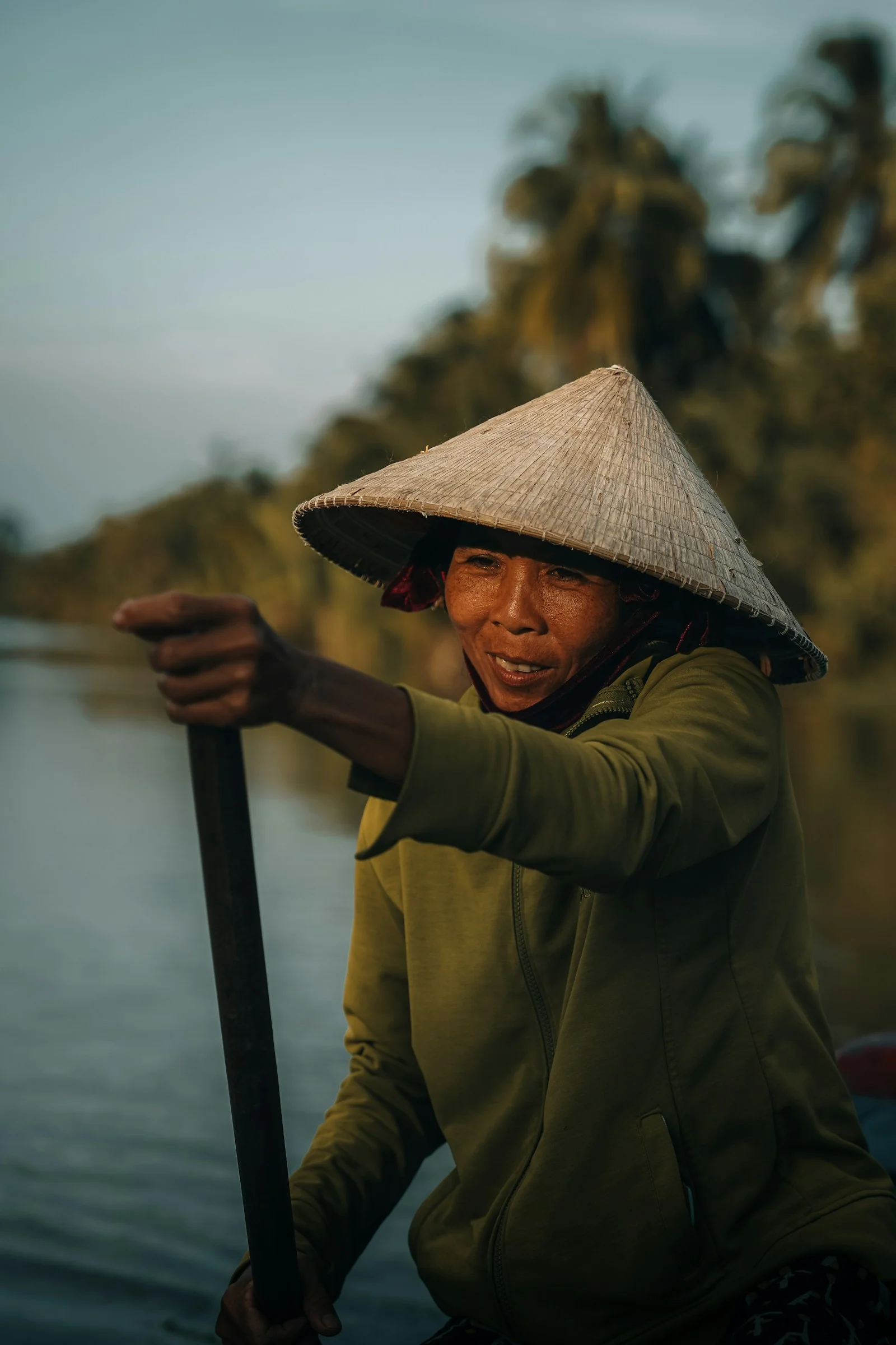 Woman paddles a boat wearing a conical hat