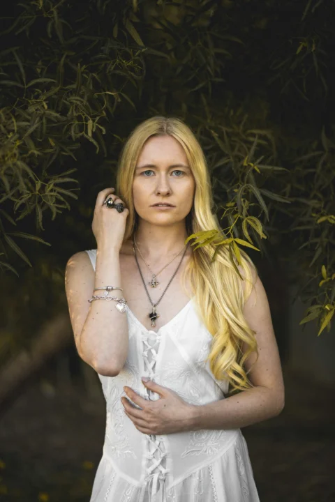 A blonde woman poses in front of foliage
