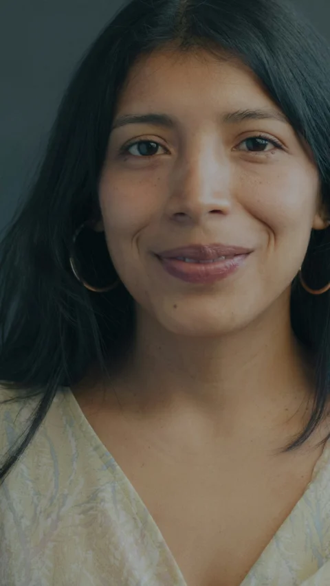 A woman with long dark hair wearing gold hoop earrings and a patterned top