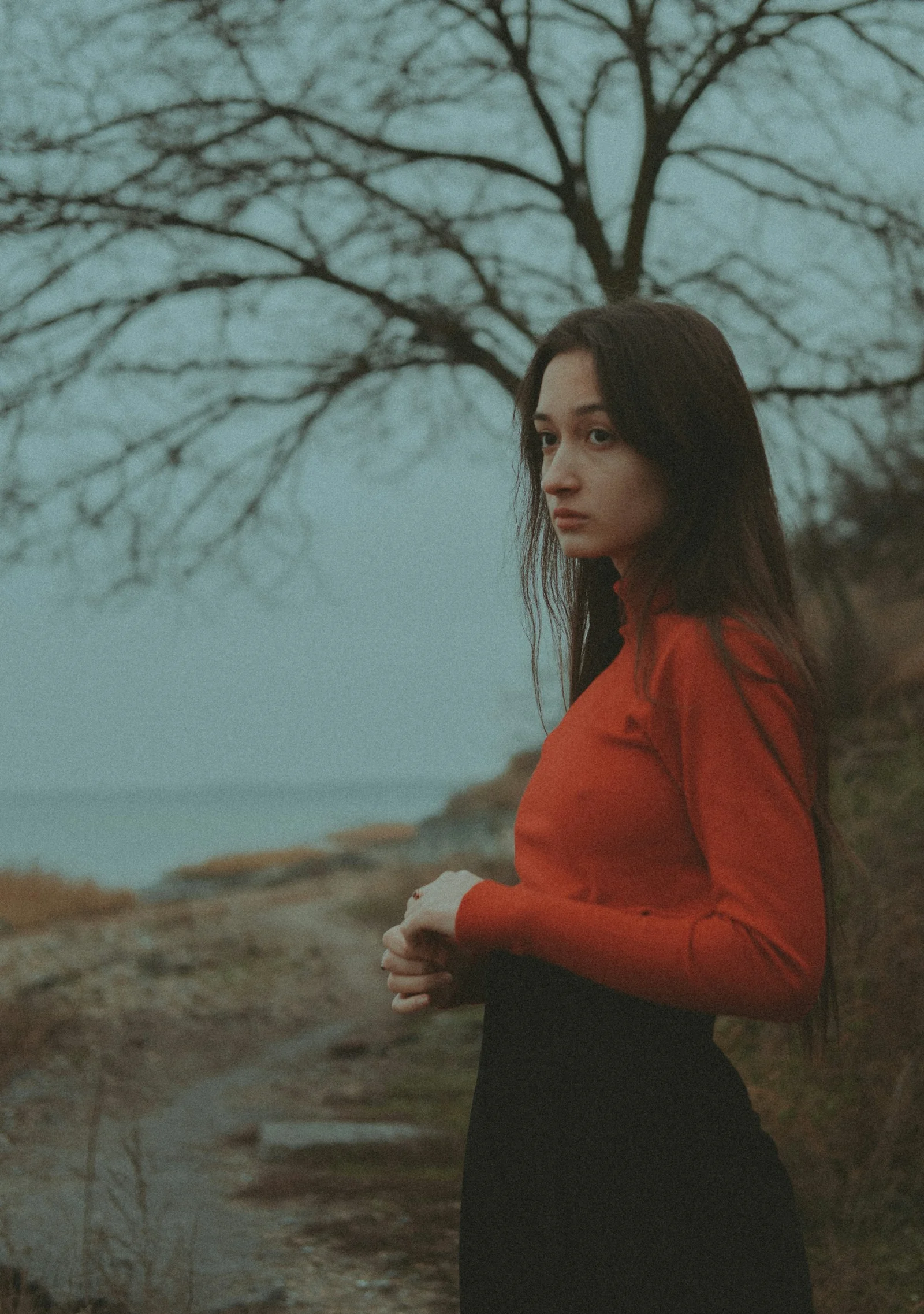 一名站在樹前的女子,背景是一片水域