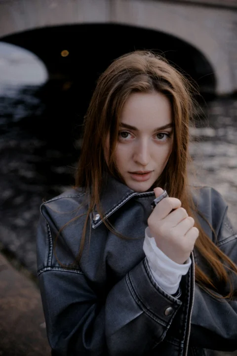 Young woman in jacket by water under bridge