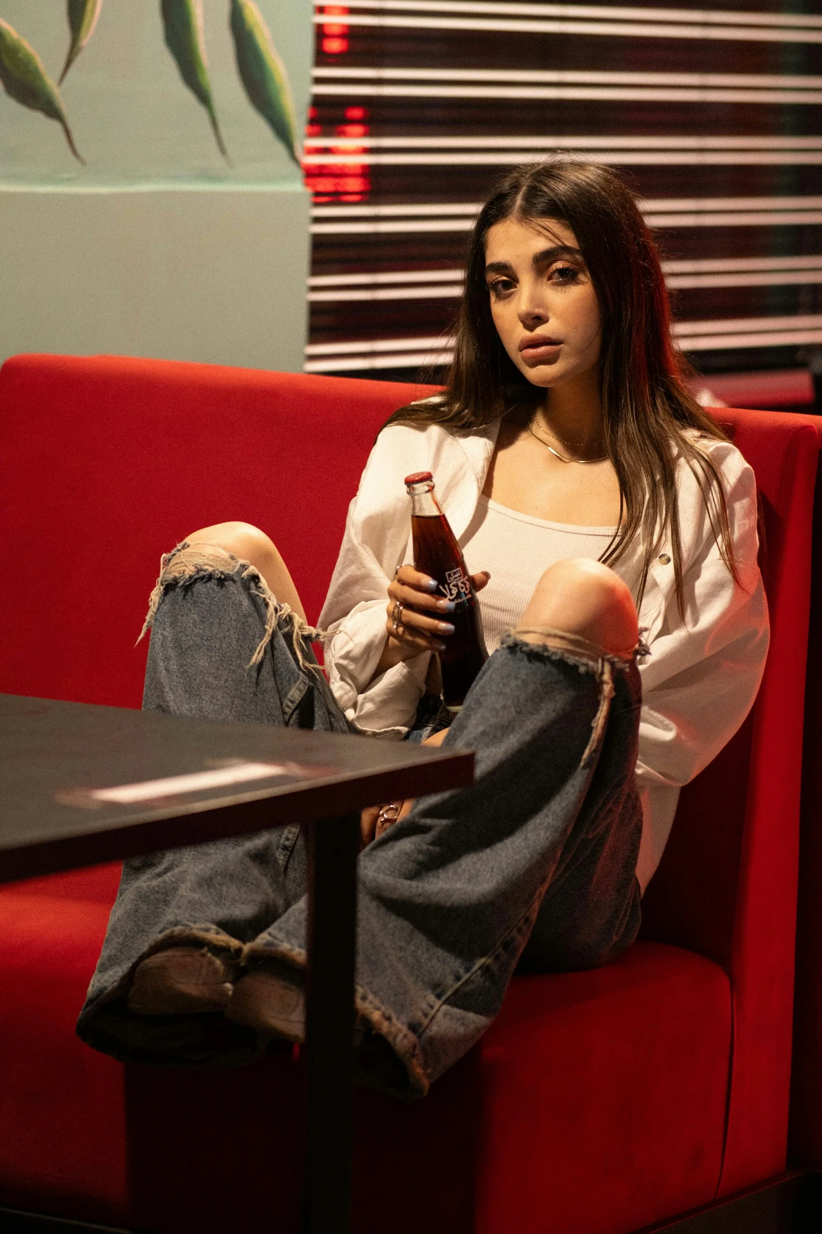 A young woman sits, holding a drink