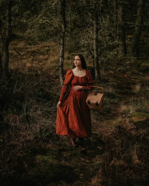 a woman in a red dress is walking through the woods