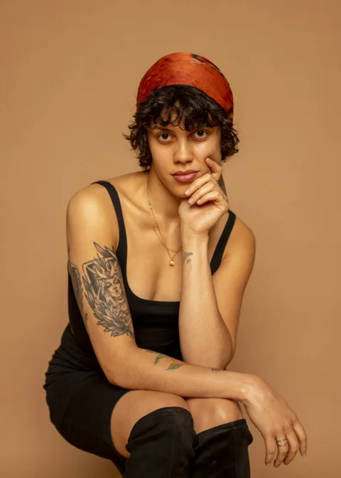 A person with tattoos and a headscarf poses