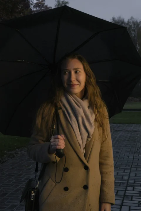 a woman holding a black umbrella on a sidewalk