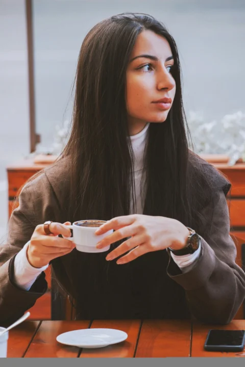 女子穿著棕色外套,手拿白色陶瓷馬克杯