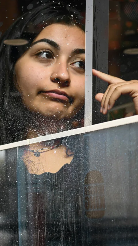A woman contemplates through a window, thoughtfully