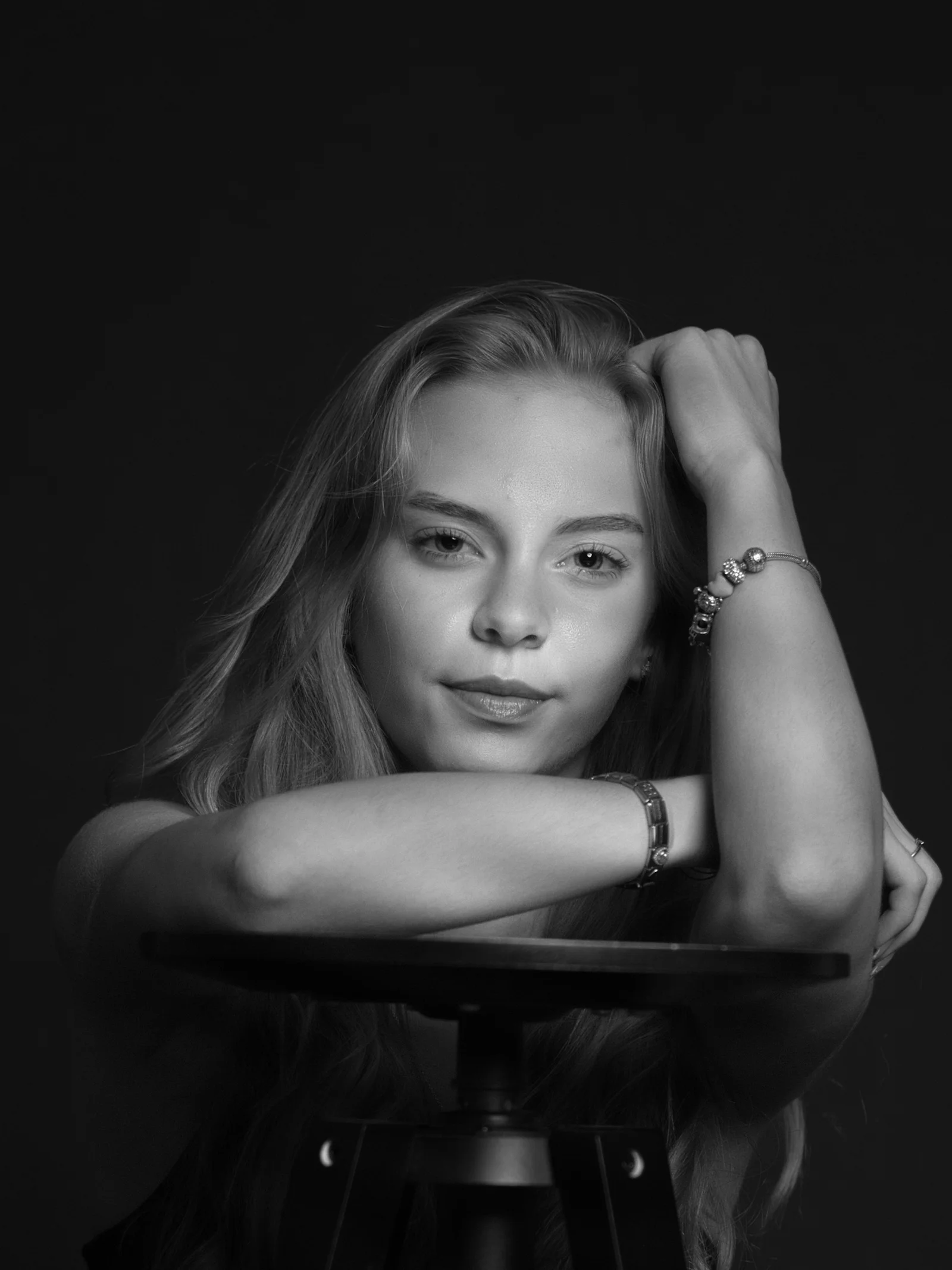 Young woman with long blonde hair resting arms on stool