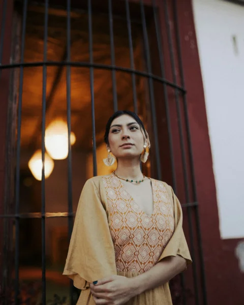 Woman in a dress poses by a barred window