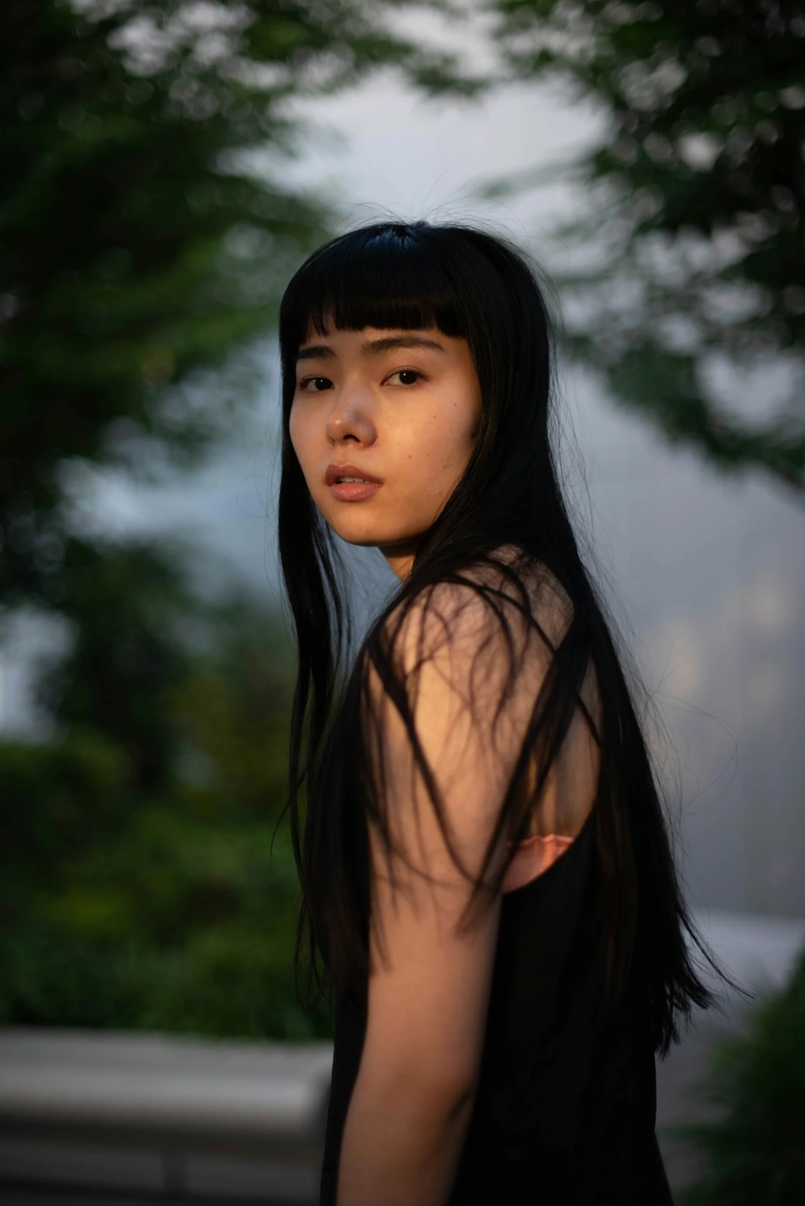 긴 검은 머리를 한 여성이 나무 앞에 서 있는 모습