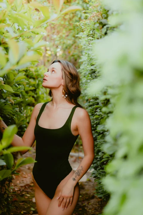 a woman in a black swimsuit standing in a bush