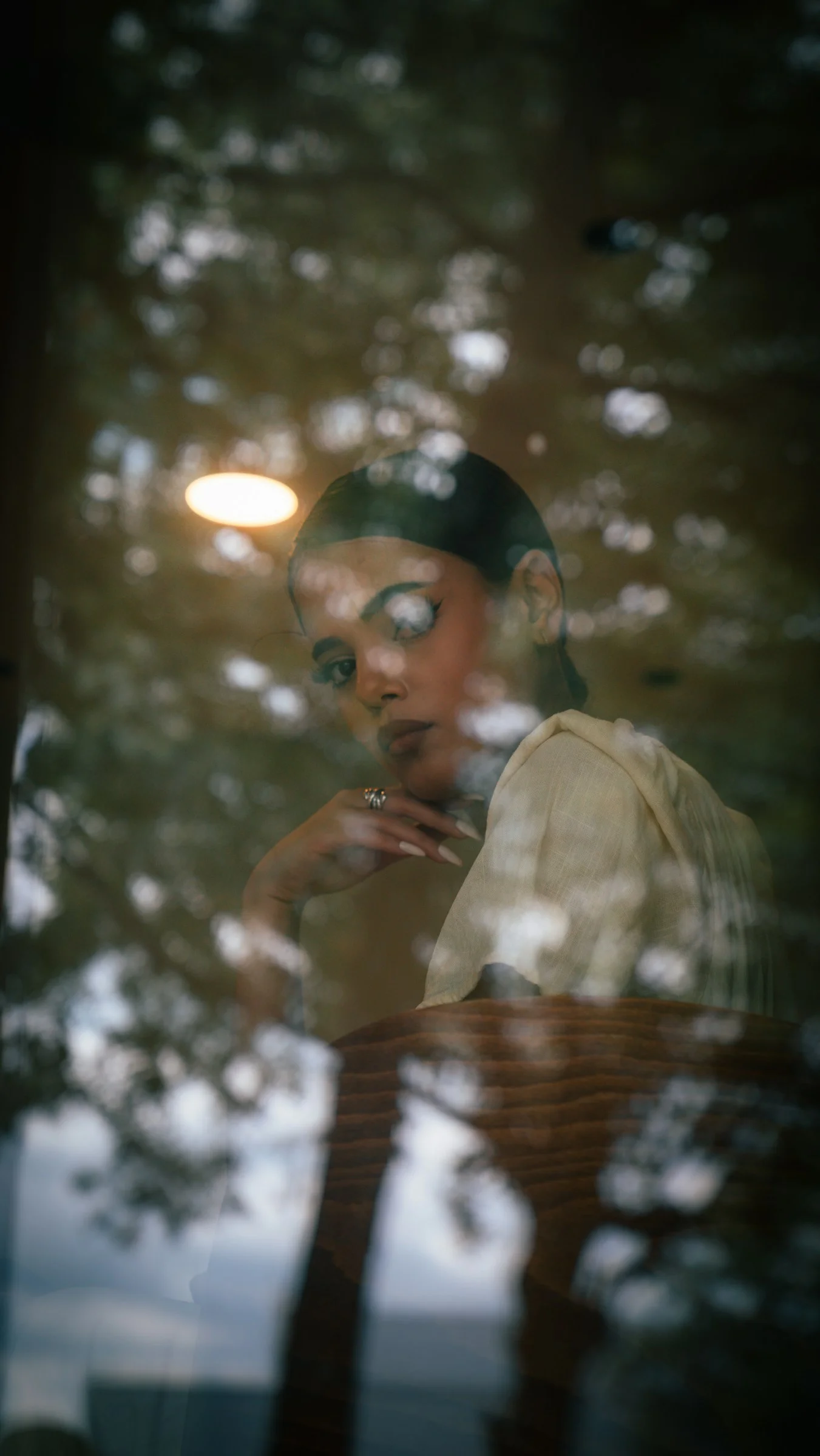 A woman with dark hair and winged eyeliner reflected in a glass window