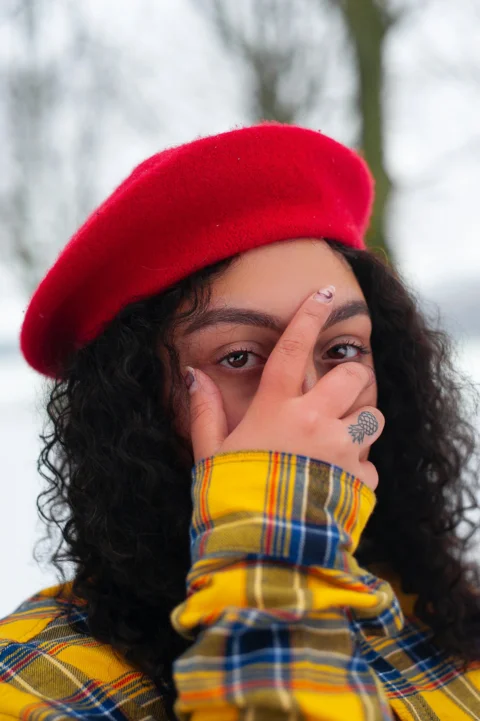 woman wearing yellow, brown, and blue plaid long-sleeved shirt with red hat holding her face