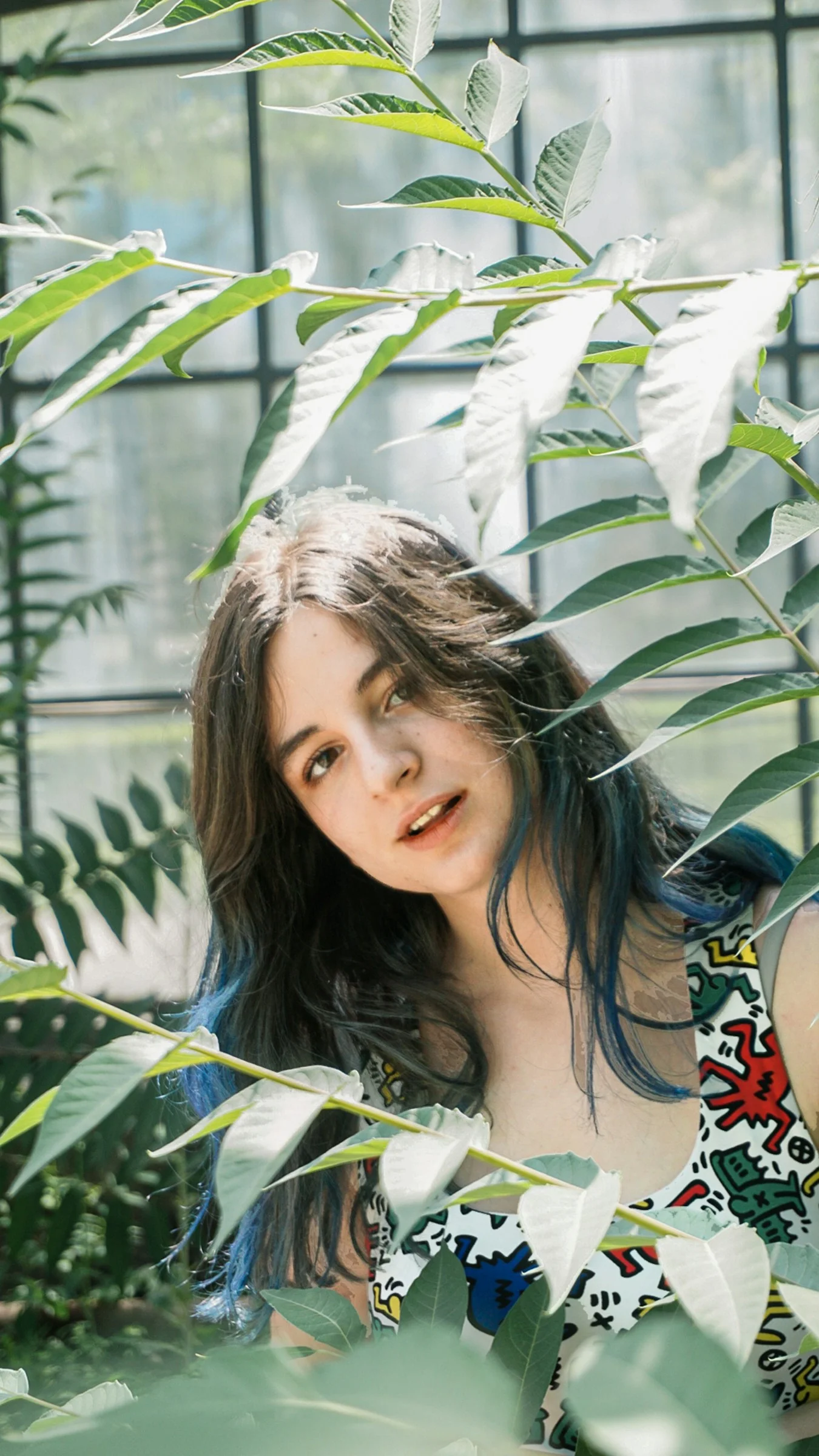 a woman standing in front of a window surrounded by plants