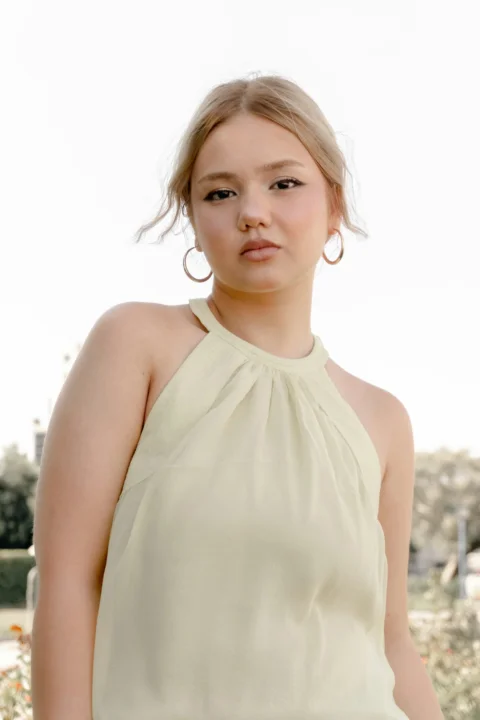 A young woman with blonde hair wearing a pale yellow halter top and hoop earrings