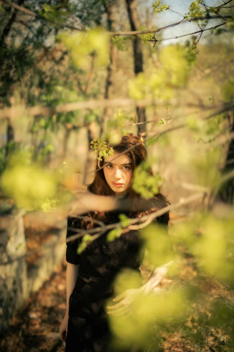A woman in a black dress framed by blurred green spring branches