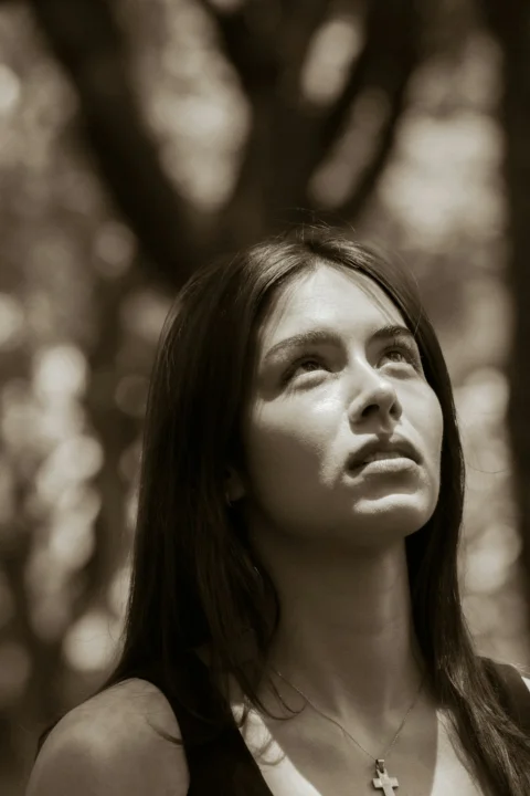 Young woman with cross necklace looking up in sepia tone