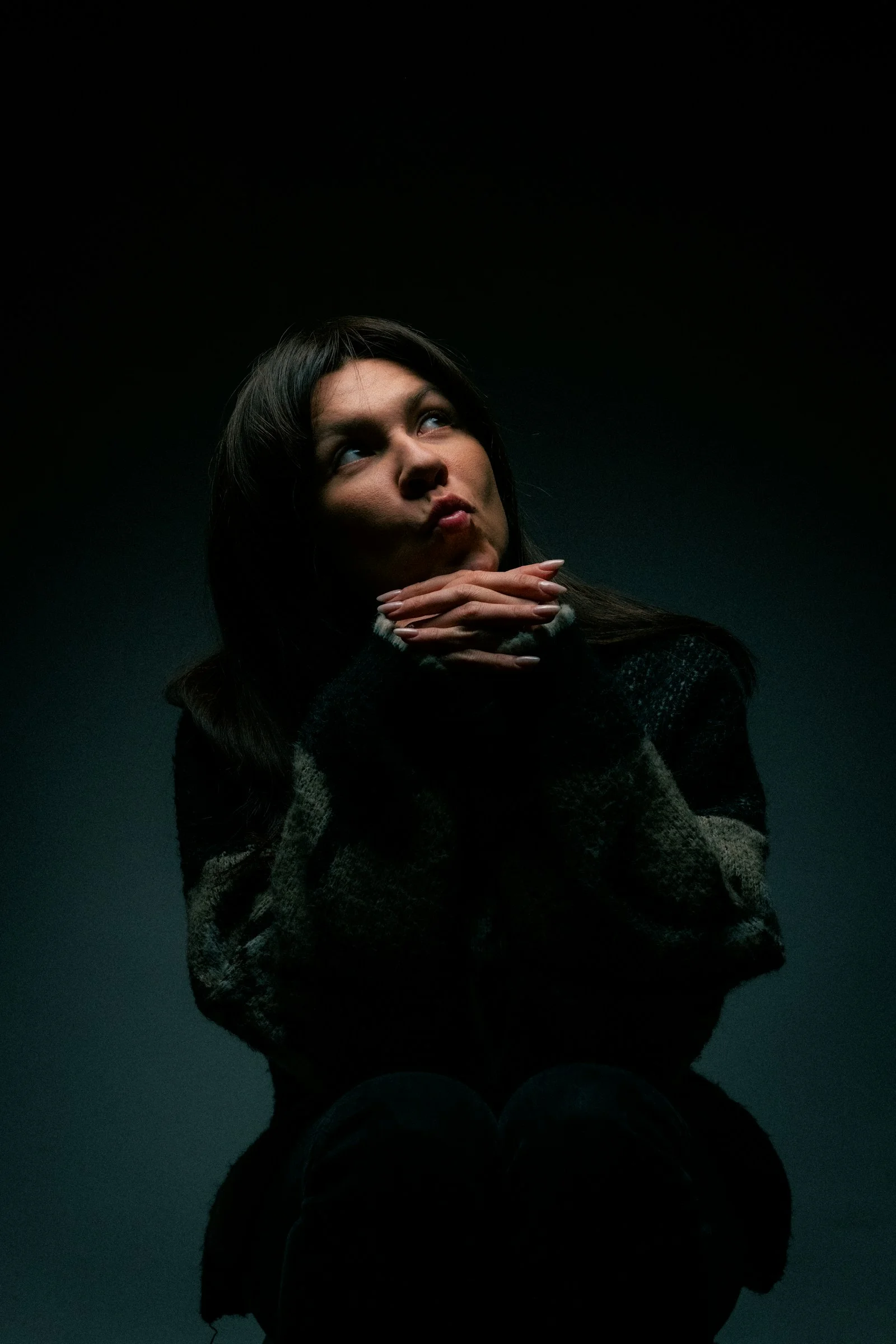 A woman sitting in the dark with her hands on her chest