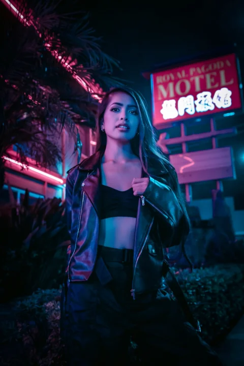 夜、赤と白のネオンサインのそばに立つ黒いレザージャケット姿の女性