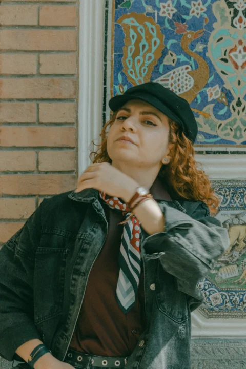 A woman with curly red hair wearing a black cap and denim jacket