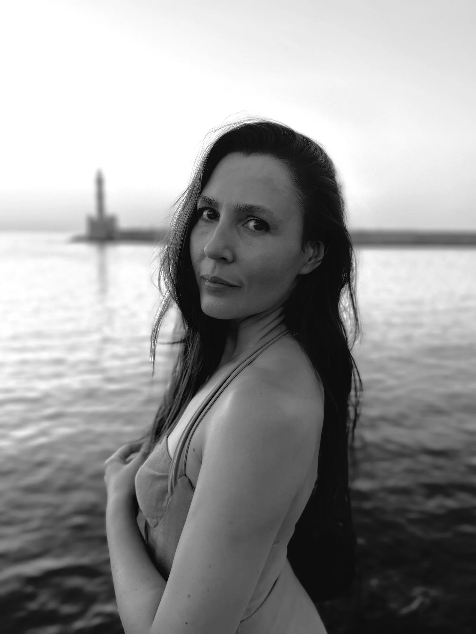 A woman with long dark hair looking back over her shoulder by the sea